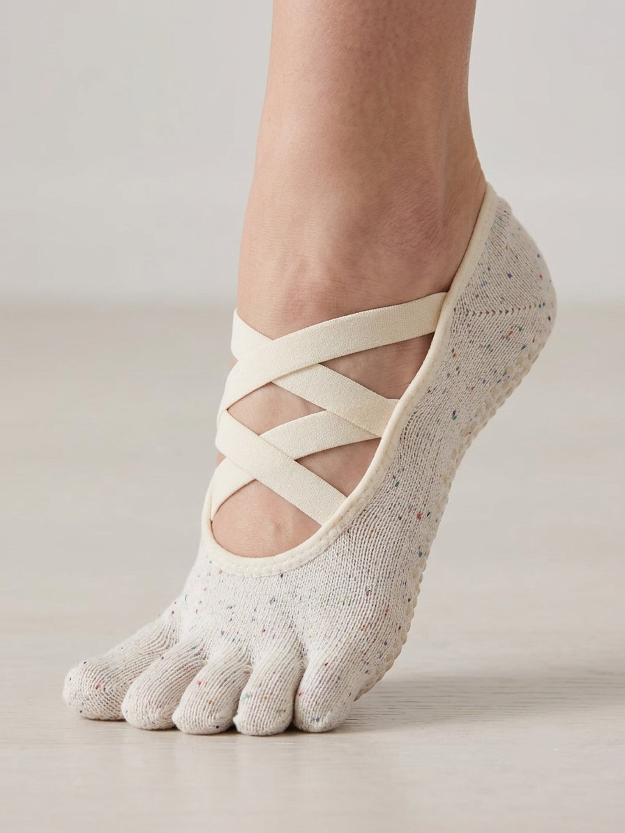 Ivory speckled five-toe Pilates grip socks by ARCHE with ballet-inspired crisscross straps, worn for reformer Pilates and studio workouts