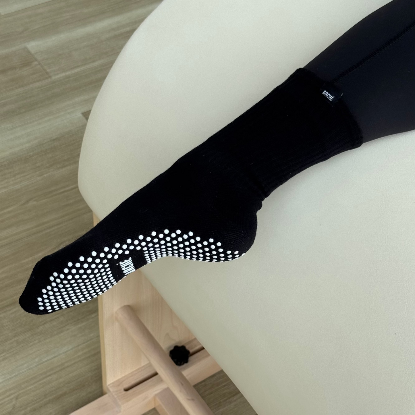 Black ARCHÉ crew Pilates grip sock worn on foot, showing white non-slip sole grips.