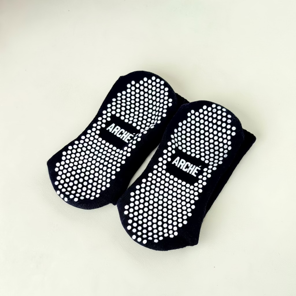 Sole view of black ARCHÉ Pilates grip socks with white non-slip grip dots for yoga, barre and studio workouts.