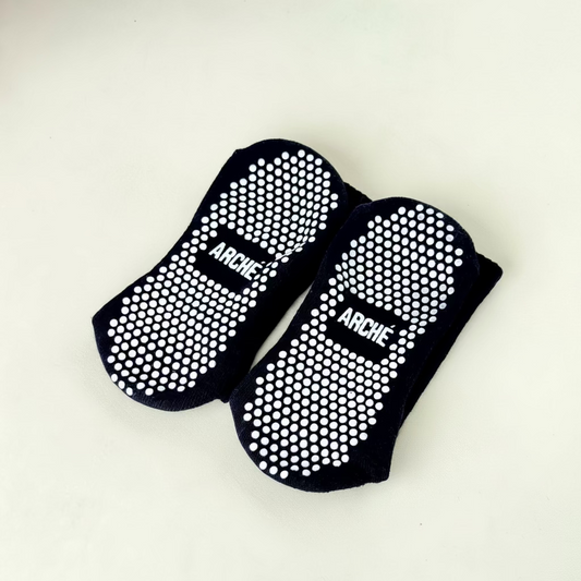 Sole view of black ARCHÉ Pilates grip socks with white non-slip grip dots for yoga, barre and studio workouts.