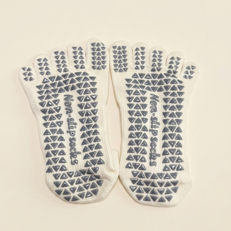 Bottom view of ARCHE cream five-toe grip socks featuring full-sole non-slip grips for added traction during studio workouts.