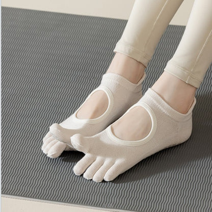 ARCHE cream five-toe reformer Pilates grip socks worn on a textured studio mat, featuring a minimalist open-top cutout design.