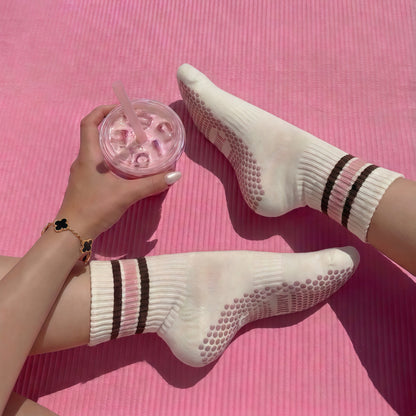 Model wearing ivory ARCHÉ striped Pilates grip socks with pink non-slip soles on a yoga mat.