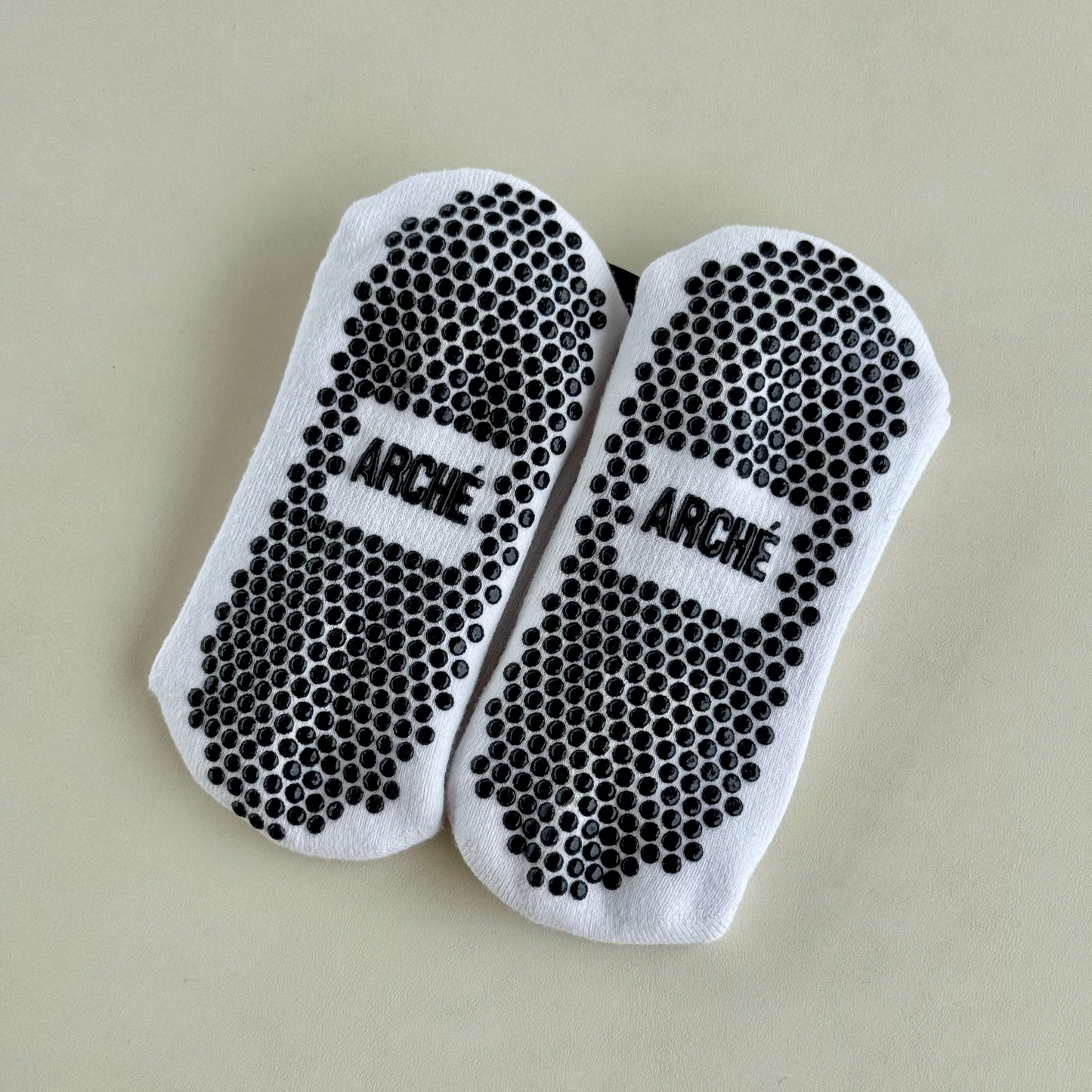 Sole view of white ARCHÉ crew Pilates grip socks with black full-sole non-slip grip dots.