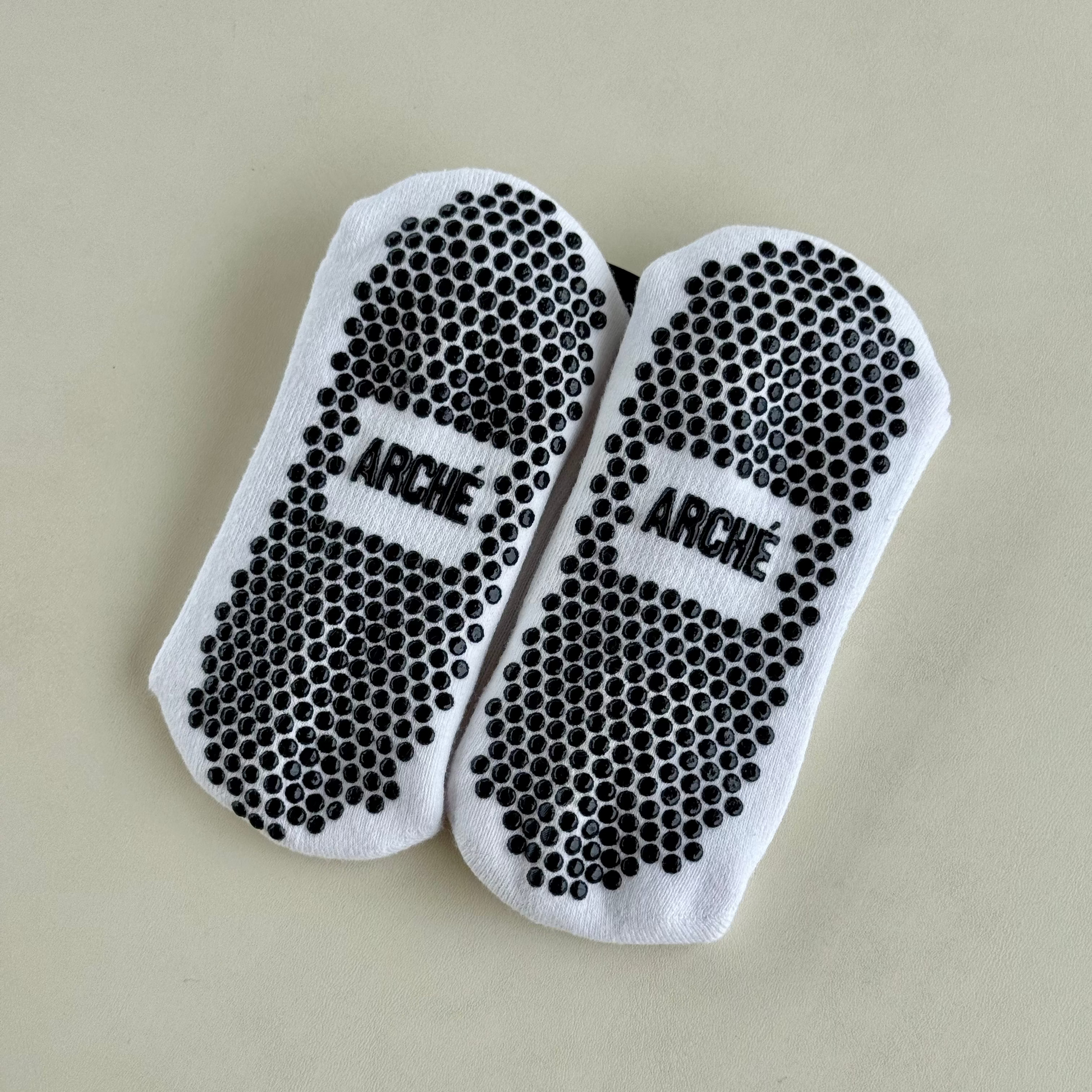 Sole view of white ARCHÉ crew Pilates grip socks with black full-sole non-slip grip dots.